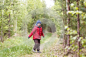 Cute boy in red hat and warm pants in forest