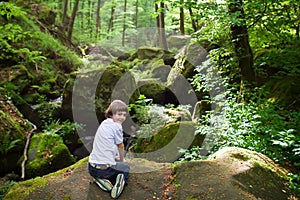 Cute boy on the rocks near a scenic waterfall