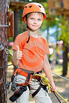 Cute boy shows thumb up with climbing equipment in