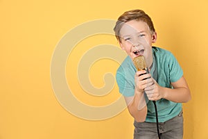 Cute boy singing in microphone on color background