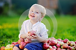 Cute boy sitting on heap of apples and eating ripe apple