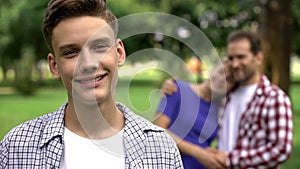 Cute boy smiling on background of cheerful hugging parents, supporting family