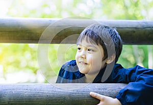 Cute boy with smiling face looking out, Candid shot happy kid playing in the park,Child having fun in a climbing on wooden fame