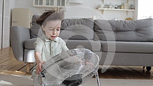 Cute boy suffering from summer heat enjoy fresh cool breeze blowing from retro fan air conditioner