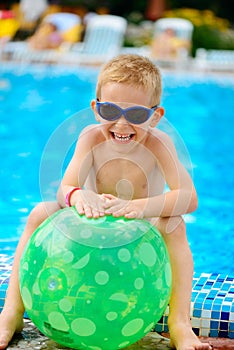 Cute boy in sunglasses sitting at pool