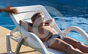 Cute boy taking sun near a swimming pool