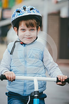 Cute boy of three years old in a blue vest and protective helmet rides a bike run along a city street. Children`s useful games in