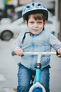 Cute boy of three years old in a blue vest and protective helmet rides a bike run along a city street. Children`s useful games in