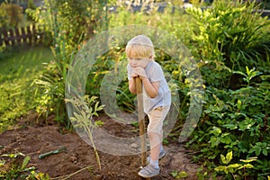 Cute boy tired dig shoveling and rested in backyard at summer sunny day. Mommy`s little helper