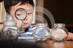 Cute boy using a magnifying to find money coins in glass,saving