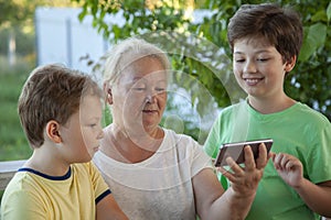 Cute boy using smartphone with grandma at home veranda