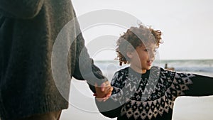 Cute boy walking coast holding mother hand. Smiling child talking unknown parent