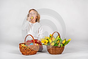 Cute boy with wavy hair sits on a white background next to a basket with Easter eggs