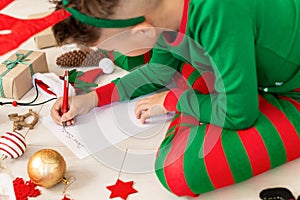 Cute boy wearing christmas pajamas writing letter to Santa on livingroom floor. Overhead view of a young boy writing wish list.