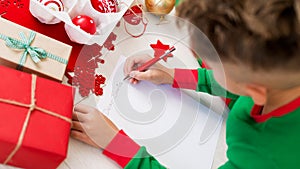 Cute boy wearing christmas pajamas writing letter to Santa on livingroom floor. Overhead view of a young boy writing wishlist.