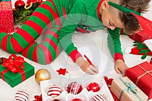 Cute boy wearing christmas pajamas writing letter to Santa on livingroom floor. Overhead view of a young boy writing wishlist.