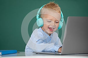 Cute boy wearing headphones, study with laptop in classroom, listening audio lesson course. Education, school