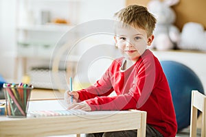 Cute boy wearing red sweater sitting at small wooden table