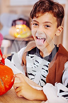 Cute boy wearing skeleton costume for Halloween party coloring pumpkin