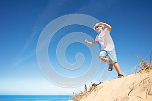 Cute boy in white jump from sand dune on a beach