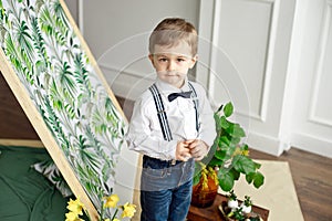 Cute boy in a white shirt and bow tie stands in a room near the tent with a smile.