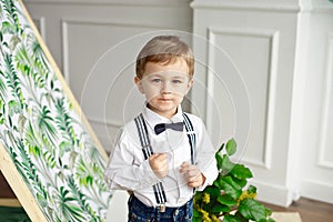 Cute boy in a white shirt and bow tie stands in a room near the tent with a smile.