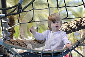 A cute boy in a white shirt lies in a hammock. The child is resting