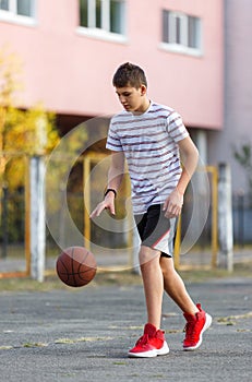 Cute boy in white t shirt plays  basketball on street  playground. Teenager  throws orange basketball ball outside. H
