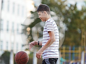 Cute boy in white t shirt plays  basketball on street  playground. Teenager  throws orange basketball ball outside. Hobby,