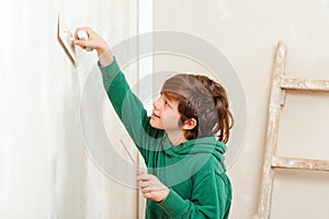 Cute boy working with spatula. Home renovation. Cute son helps parents to repair room