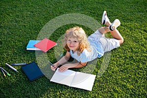 Cute boy writing on notebook on green grass.