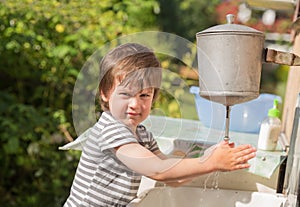 Cute boy washes his hands under washstand