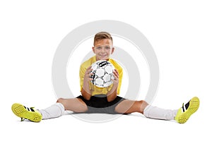 A cute boy in a yellow sports uniform holds a ball in his hands, young footballer isolated on a white background.