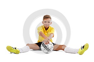 A cute boy in a yellow sports uniform holds a ball in his hands, young footballer isolated on a white background.