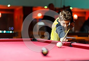 Cute boy in yellow t shirt plays billiard or pool in club. Young Kid learns to play snooker. Boy with billiard cue