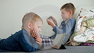 cute boys are concentrated on playing games and watching videos on internet use modern gadgets smartphone and tablet