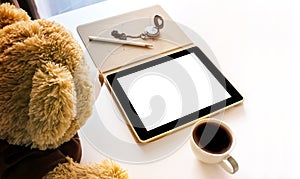 Cute brown bear doll looking tablet on table with coffee cup