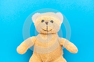 Cute brown teddy bear child toy with visible upper body and open arms isolated in a seamless pastel baby blue coulor