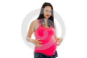 Cute brunette pregnant woman in bright pink shirt touching her belly isolated on white background
