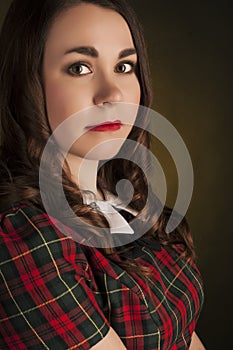 Cute brunette in tartan dress with red lips and curles. Studio portrait