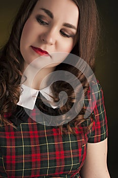 Cute brunette in tartan dress with red lips and curles. Studio portrait