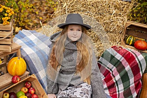 Cute brunette teen girl in black hat and gray coat near autumn elements decoration - pumpkins, apples, plaid, hay. Cosiness,