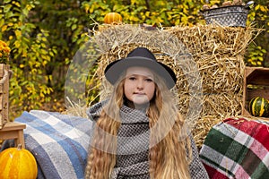 Cute brunette teen girl in black hat and gray coat near autumn elements decoration - pumpkins, plaid, hay. Cosiness, autumn
