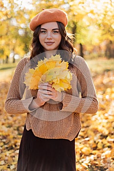 Cute brunette woman holding autumn leaves in the nature, looking at camera.