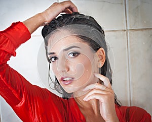 Cute brunette woman with perfect body posing in erotic pose under shower with wet hair and transparent red shirt