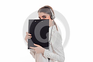 Cute brunette woman working in call center with headphones and microphone hide her smile behind a blackboard isolated on