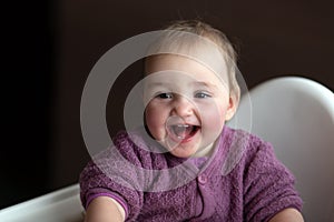 Cute carefree laughing baby sitting on baby chair. Baby is wearing lilac knitted overall