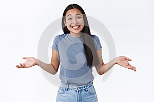 Cute carefree, relaxed smiling asian woman shrugging, tilt head silly and spread hands sideways indesicive, dont care