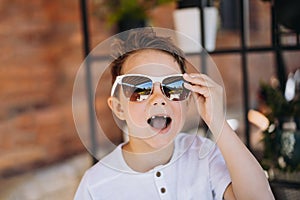 Cute cauasian boy in white tee shirt and sunglasses posing for camera and showing his lost tooth. photo