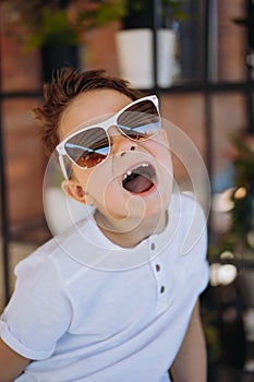 Cute cauasian boy in white tee shirt and sunglasses posing for camera and showing his lost tooth. photo